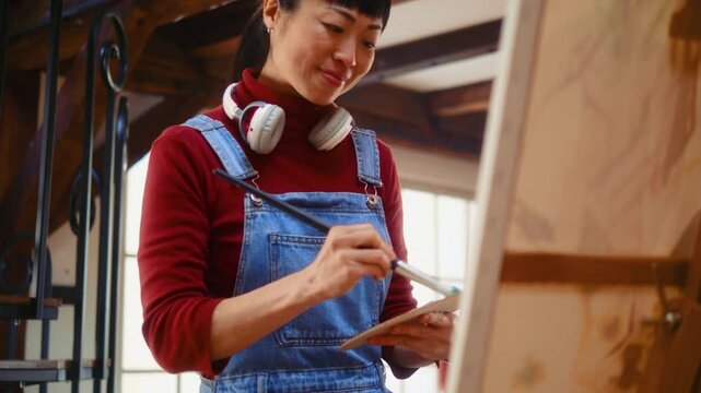 Hapy Japanese woman artist painting on an easel at home with satisfied emotion.
