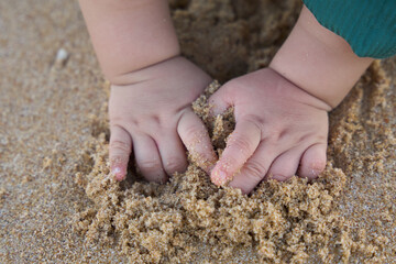 The baby is playing with sand, and the baby's hands are in it. The baby has its fingers in the sand, and it seems to be enjoying itself.