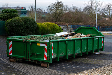 A green dumpster is located in an urban setting, filled with various construction debris and...