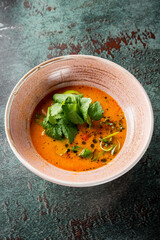 A vibrant bowl of spicy soup garnished with fresh cilantro and lime, set against a textured dark background. The contrasting colors create an appetizing visual.