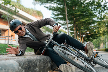 Asian Businessman falling off bicycle in city. Accident Injury leg pain. Broken leg Cyclist falls...