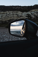 Beach scene is reflected in the side mirror of a parked car, capturing the ocean waves and evening...