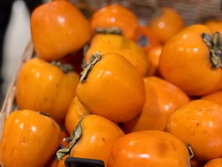A pile of ripe juicy orange flat persimmons in a box, offered for sale at a supermarket vegetable stand, demonstrates organic, vegetarian and healthy food. Close-up