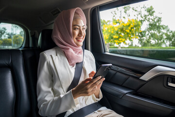Asian muslim Woman Traveler sitting in car back seats using smartphone call taxi service in application and put on safety belt. Female islamic passenger in car traveling to destination.