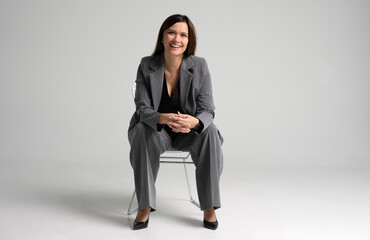Portrait of a cheerful young businesswoman sitting in a chair against white background.
