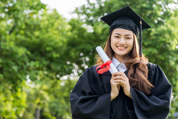 Happy asian woman in graduation costume with cap standing outdoor public park. College degree...