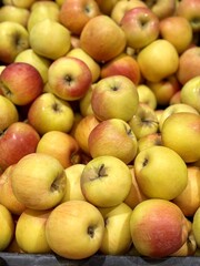A mound of large red yellow coloured apples in boxes is displayed in the window of the supermarket's vegetable stand, demonstrating organic, vegetarian and healthy food. Close-up