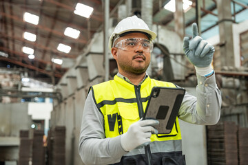 Confident engineer man with safety helmet standing analyzing with tablet in factory warehouse....
