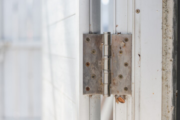 a door hinge attached to a white door frame. The hinge is metallic and has multiple screws securing it to the door and the frame.