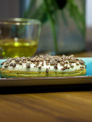 Chocolate covered pastry sits on a plate next to a cup of tea