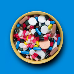 Pile of pills in a bowl on a blue background, top view. The concept of filling natural products with medicines