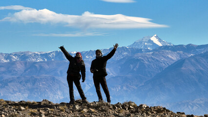 Pareja en la cima de una montaña con el Aconcagua y la cordillera de los andes de fondo