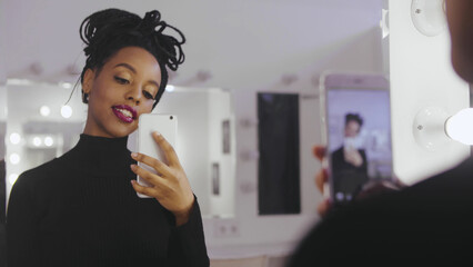 Beauty model photographing its reflection in makeup mirror on mobile phone
