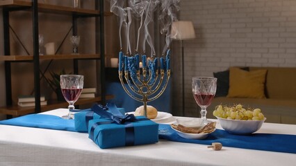Shot of festive table with food and drinks in a jewish home for traditional hanukah celebrations, gift boxes and menorah with blown off candles on the table.
