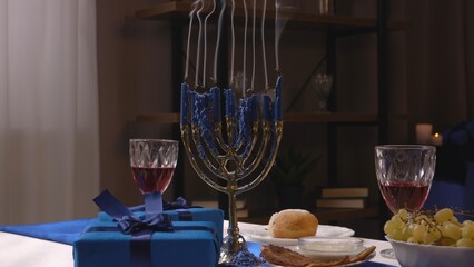 Shot of festive table with food and drinks in a jewish home for traditional hanukah celebrations, gift boxes and menorah with blown off candles on the table.