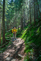 Obraz premium Young mountaineer trekking through a lush forest trail on a sunny day, looking away and contemplating the journey.