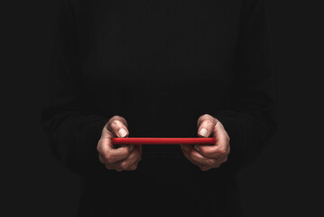 Close up of a hacker's hands holding a red cell phone on a black background