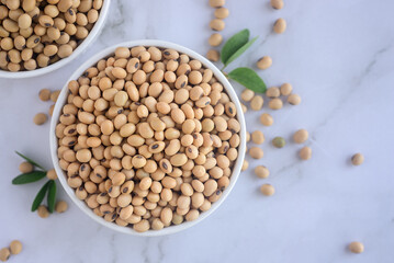 Dried soy beans or soya beans in a ceramic bowl on white table background, top view image.
