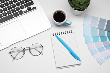Designer's workplace with stationery, color palettes, cup of coffee and laptop on grey table, flat...