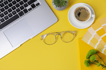 Designer's workplace with laptop, stationery and cup of coffee on yellow background, flat lay