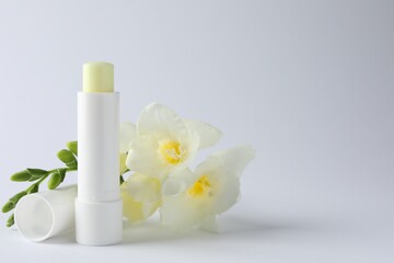 Lip balm and freesia flowers on white background, closeup. Space for text