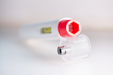 A used pen injector with a red tip for biological treatments such as Adalimumab, Etanercept or epinephrine. One is standing on a white light background, aseptic, clean, white and well lit.
