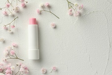 Moisturizing lip balm and gypsophila flowers on light textured table, flat lay. Space for text