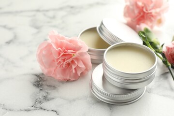 Moisturizing lip balms and pink flowers on white marble table, closeup