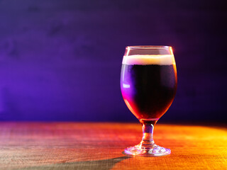 Glass of dark craft beer on a wooden table. Colored light, copy space