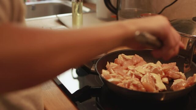 Professional chef searing marinated chicken breast cubes in hot skillet, sprinkling salt and turning pieces with slotted spoon while browning evenly