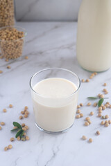 a glass of homemade soy milk with soy beans on white table background.