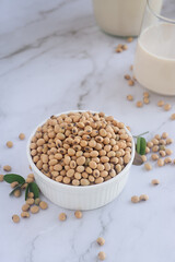 Dried soy beans or soya beans in a ceramic bowl on white table with a glass of fresh homemade soy milk.