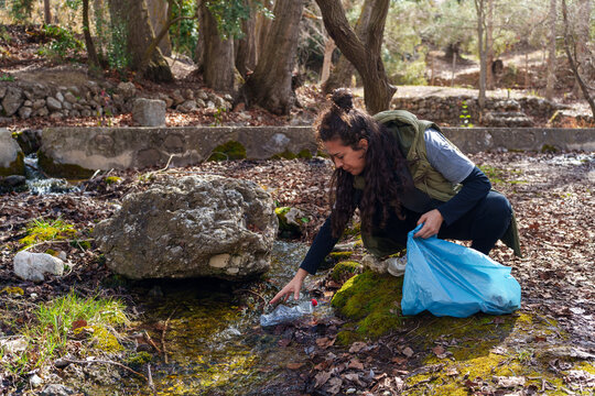 Young woman collecting plastic trash from a stream in a forest, taking care of environment