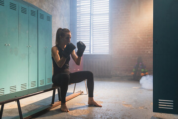 Workout in gym. Woman fighter ready for fight punching with boxing gloves in locker room. Strong...
