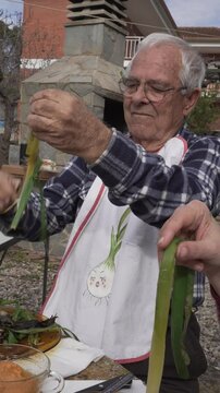 vertical video, man in his eighties drinking wine from a porr&oacute;n at an open-air cal&ccedil;otada. Dressed with a bib painted with an onion and a checked shirt.