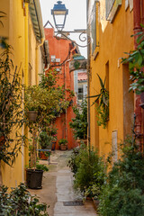 Charming Old Town Street In Menton: Narrow Cobblestone Alley With Colorful Mediterranean Buildings, Green Wooden Shutters, Hanging Laundry, Potted Plants, And Aged Facades In The French Riviera