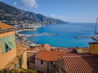 Fototapeta premium Panoramic View Of Menton On The French Riviera: Terracotta Rooftops, Sandy Beaches, Palm-Lined Promenade, And The Azure Mediterranean Sea Against A Backdrop Of Lush Green Hills And Mountains