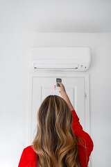 Woman holding remote control aimed at the air conditioner.