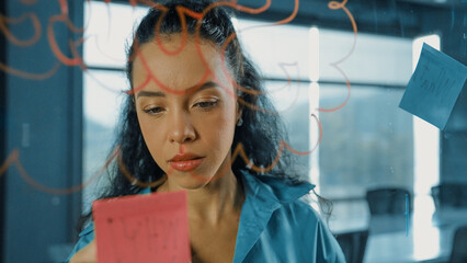 Young hispanic employee writing on colorful sticky notes. Smart businesswoman sharing marketing...