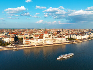 Fototapeta premium Residence of Hungarian Parliament, Budapest backdrop of sunset sunny day in summer. National symbol aerial view other bank of Danube River. Floating river pleasure passenger vessels. Travel concept