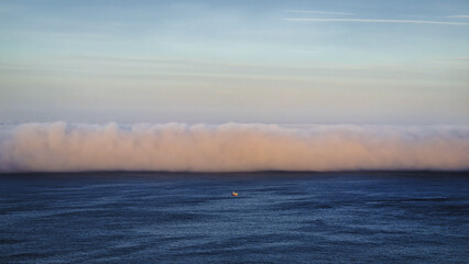 Schiff im Meer vor einer Wolkenwand bei Sonnenaufgang