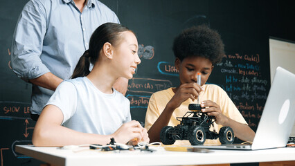 Caucasian teacher looking at laptop screen while explain car model system at blackboard with coding...