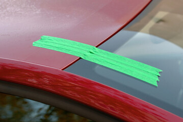Car windshield with green tape applied to the roof during repair process, indicating restoration work and replacement of the damaged auto glass. Tape securing windshield to the roof of red car