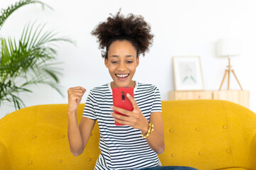 Young african woman celebrate good news looking at smartphone screen. Celebration victory concept
