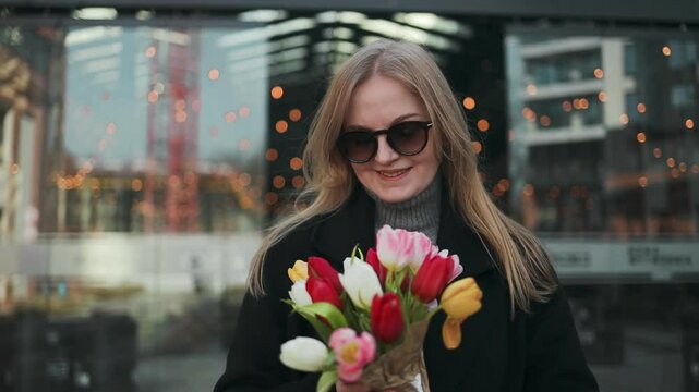 Beautiful happy Caucasian woman smelling bunch of tulips with closed eyes. High quality FullHD footage