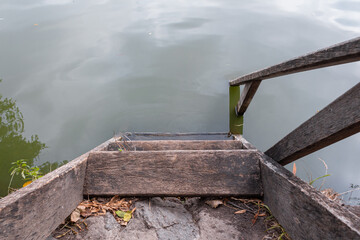 Old worn wooden brown steps with dry leaves into the lake