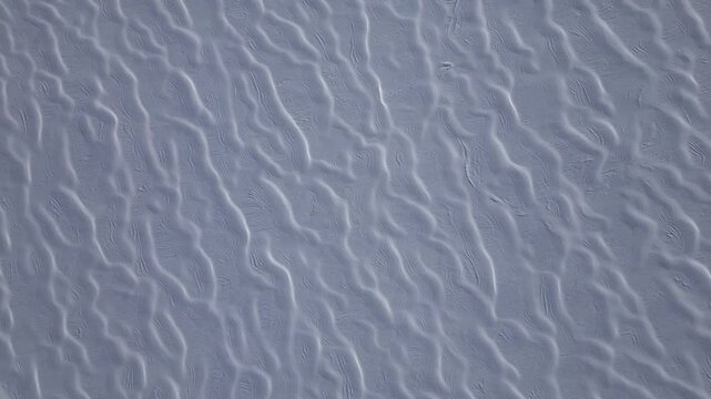 An aerial view of intricate snow formations on Glacier 3000 in the Swiss Alps. The wind has sculpted the snow into a mesmerizing pattern of parallel ridges and flowing textures. 