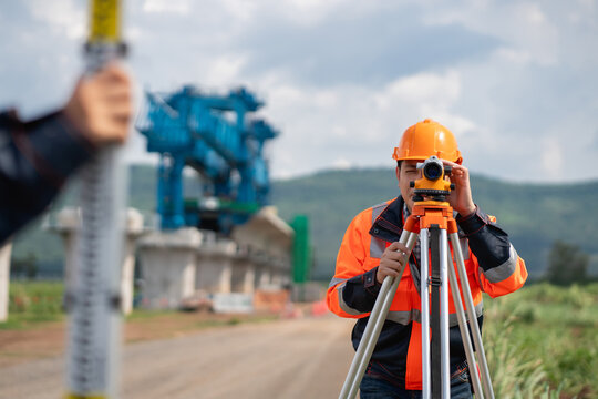 The survey team is using a theodolite and road construction plans. Civil engineers are measuring with surveying tools during the construction.