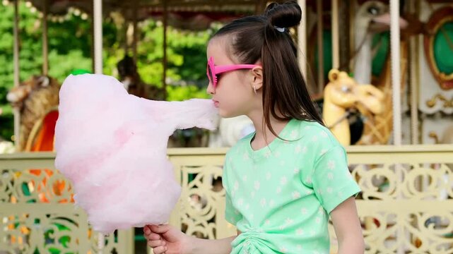A child girl in an amusement and amusement park eats cotton candy in summer, International Children's Day, happy childhood and holidays, high-quality 4k video footage