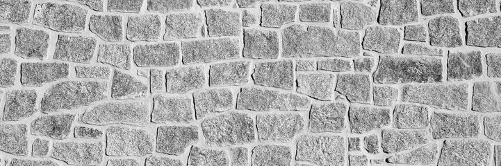 Black and white close-up of an irregular stone wall. The rough texture and natural patterns create a rustic and historical appearance. Ideal for backgrounds, textures. Long banner.